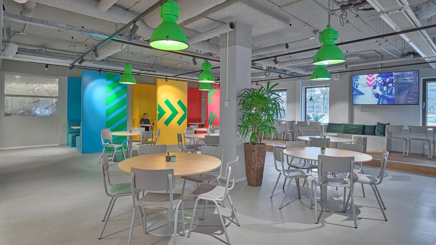 Modern office canteen with colorful wall design, tables and green ceiling lights